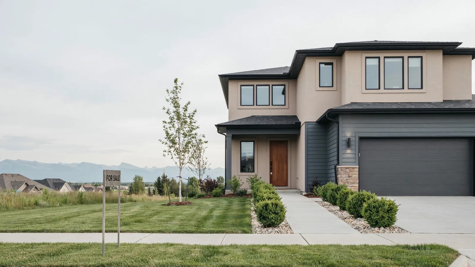A modern two storey home with mountains behind it and a for sale sign on the lawn, the Medicine Hat foreclosure guide